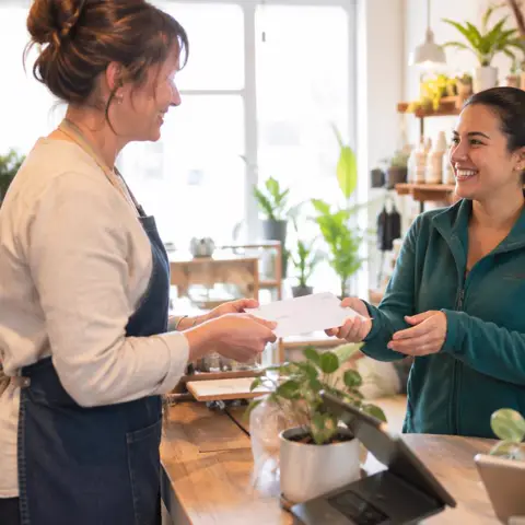 Small business owner handing an employee a paycheck in a bright shop